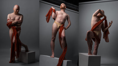 Three studio photographs of a non binary model posed on white pedestals against a gray backdrop, each draped with a red cloth. 